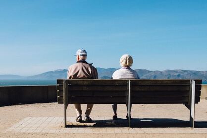 Picture of two old people sitting on a park bench overlooking mountains